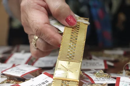A hand lifting a gold bracelet from a tray of price-tagged jewellery