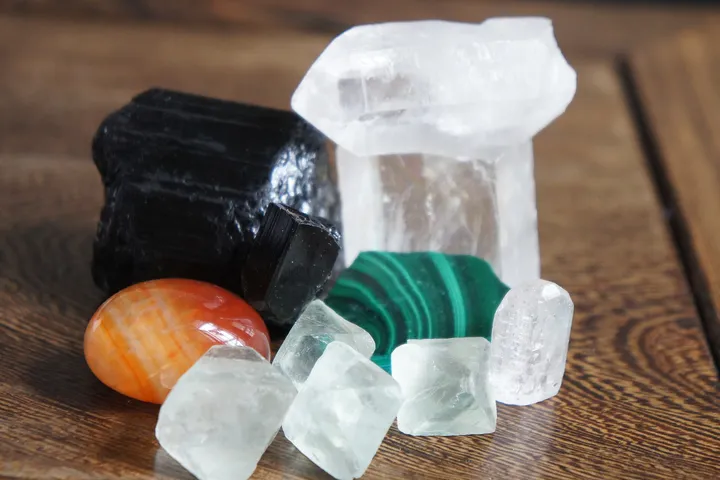 Mineral specimens grouped on a wooden table, among them a black tourmaline crystal, a quartz point and a banded carnelian pebble