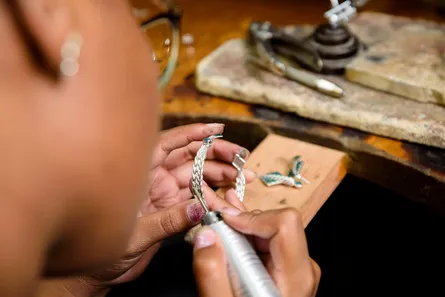 Hands forming silver links over a bench with pliers and a blowtorch