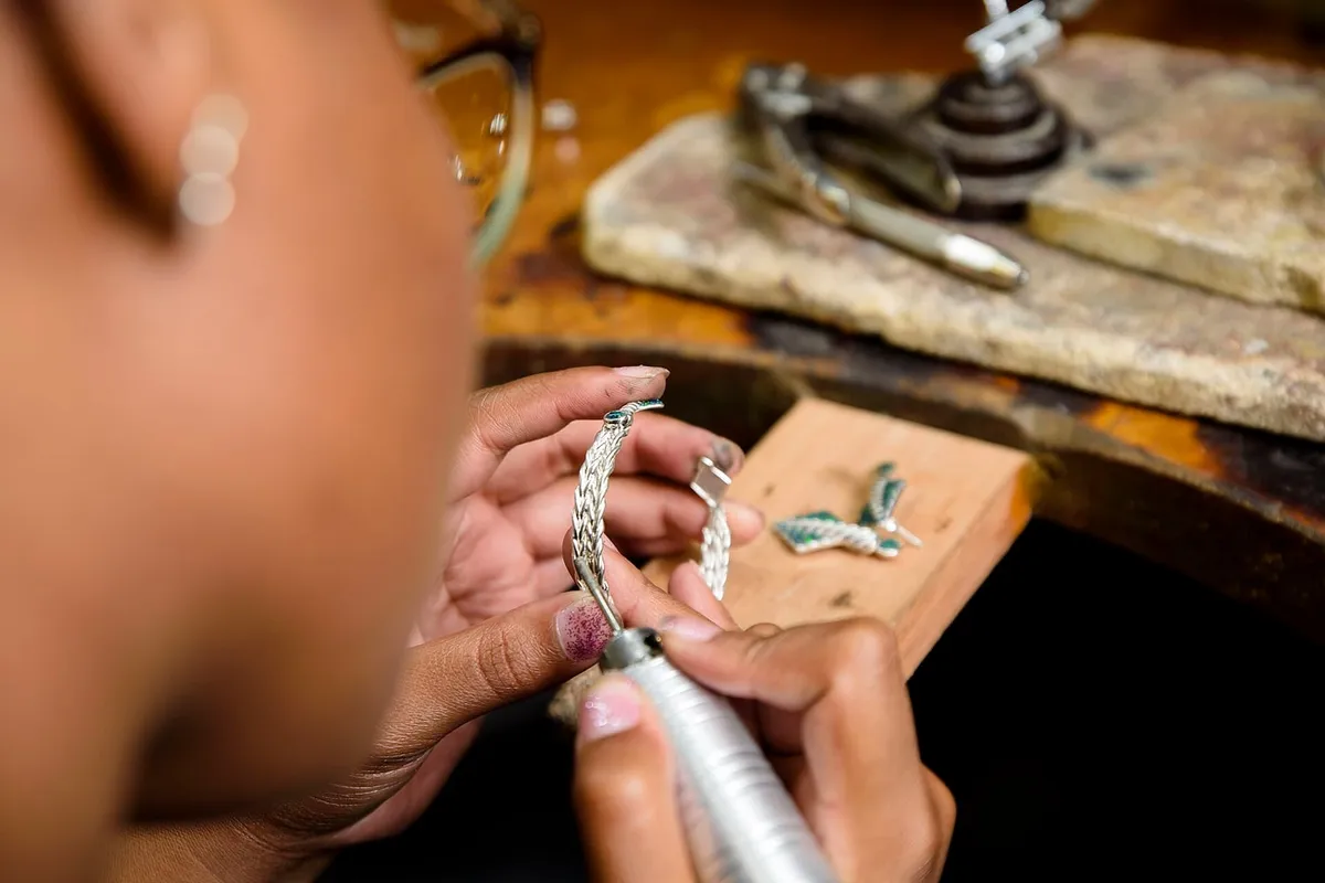Hands forming silver links over a bench with pliers and a blowtorch